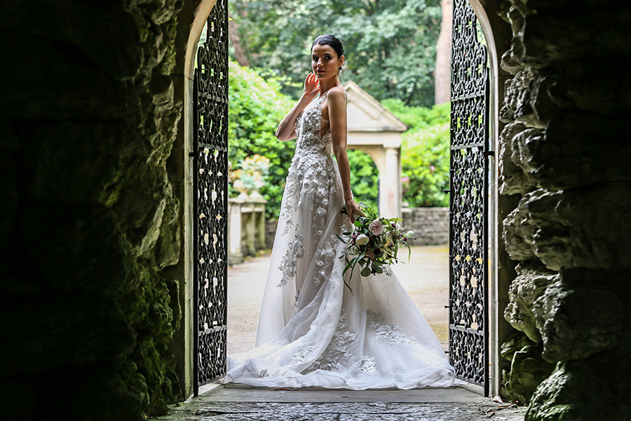 Bride wearing designer wedding dress standing in stone archway at bridal boutique photoshoot