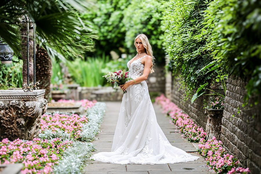 Bride wearing detailed lace wedding dress standing in formal garden walkway