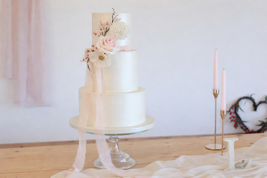 Three tier white wedding cake with sugar flowers and pink ribbon styling
