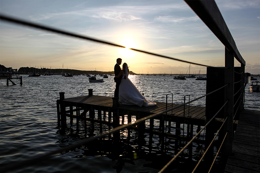 Bride and groom standing on a pier overlooking the sea at a coastal wedding venue in Dorset
