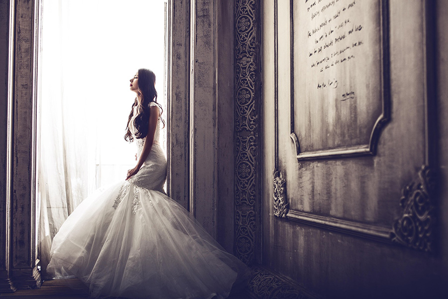 Bride wearing a fitted lace wedding dress with tulle skirt standing by a window in a Dorset bridal shop