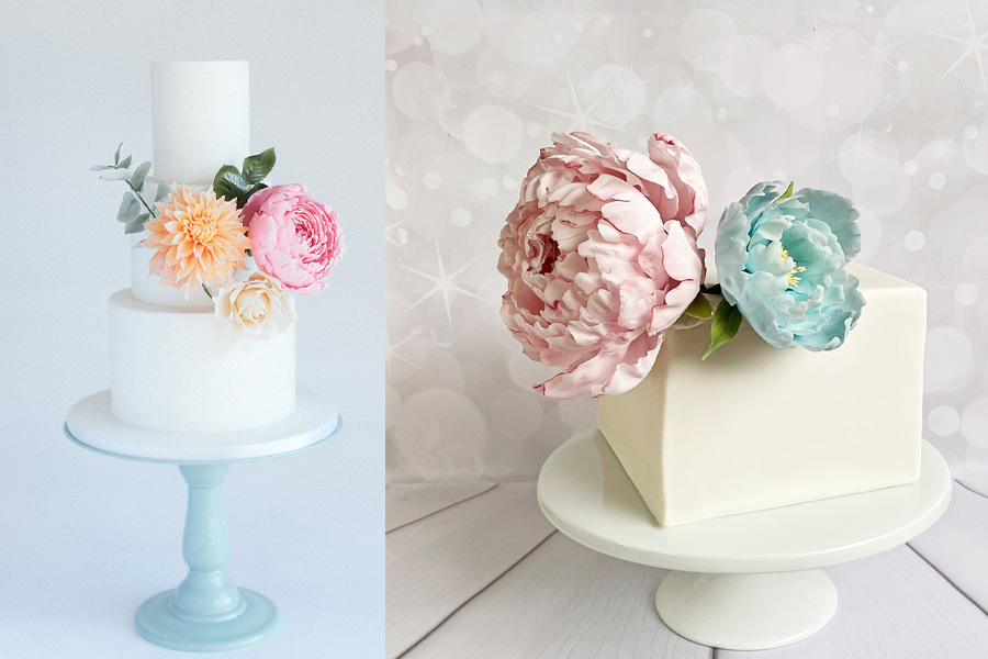 Two elegant white wedding cakes decorated with large pastel floral sugar flowers on display stands
