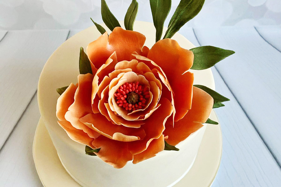 Close up of a handcrafted orange sugar flower decoration on a white wedding cake