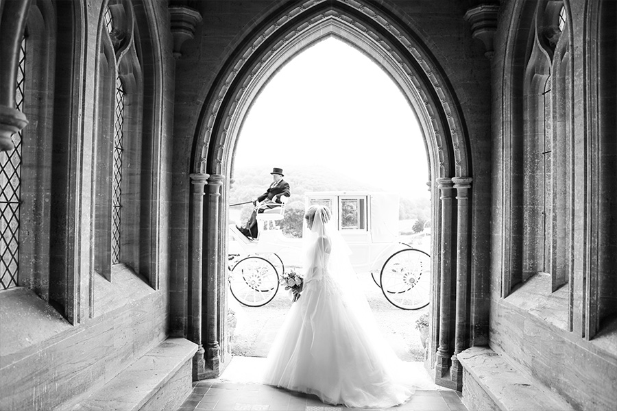 Bride standing in a grand archway at a luxury wedding venue in Dorset with carriage outside