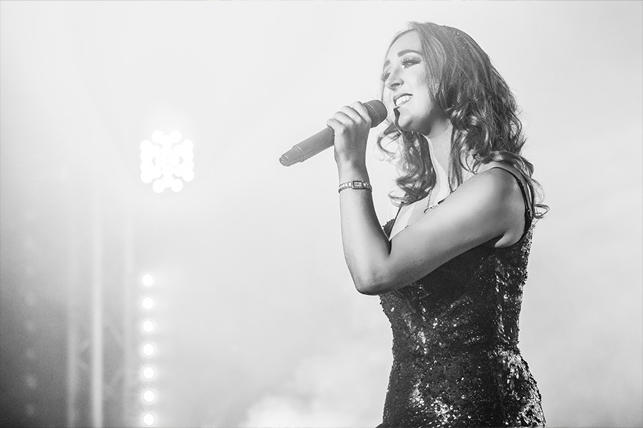 Lyndsey Cooper performing live at a wedding, singing into a microphone in a black sequinned dress under soft stage lighting