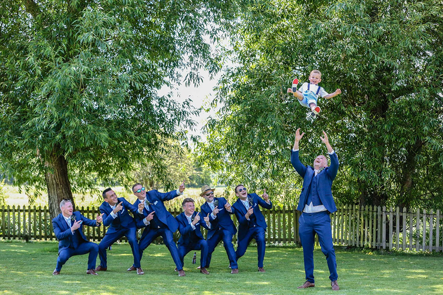 Bournemouth wedding photographer capturing groomsmen tossing baby in the air during wedding celebration