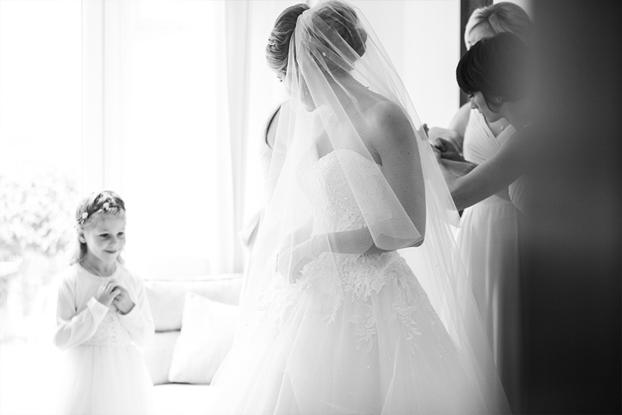 Bride having her dress adjusted during wedding morning preparations with soft natural light