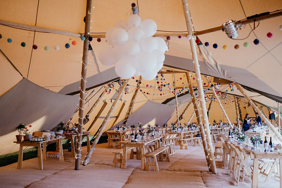 Tipi wedding interior by Coastal Tents with long tables, fairy lights and festival style decor in Dorset