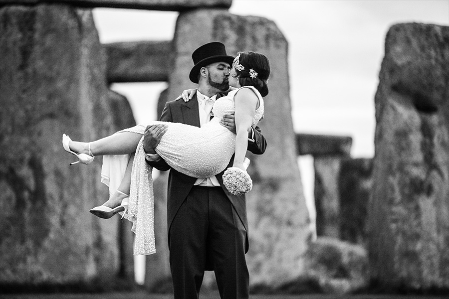 Bride and groom at Stonehenge with groom lifting bride, capturing a creative and iconic wedding portrait