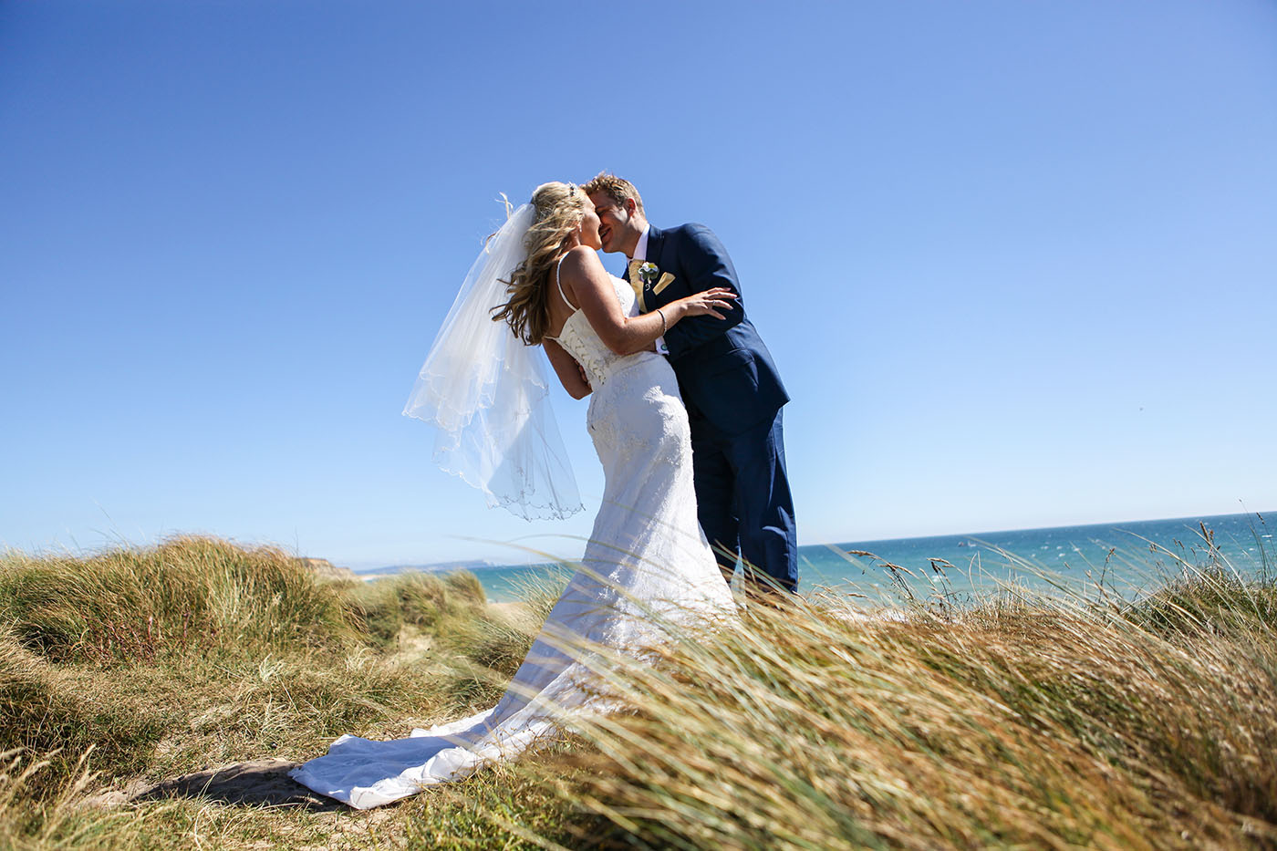 Bride and groom kissing on a coastal clifftop wedding venue in Dorset with sea views and natural landscape
