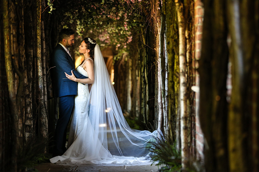 Bride and groom standing under a romantic tree lined archway at a Hampshire wedding venue