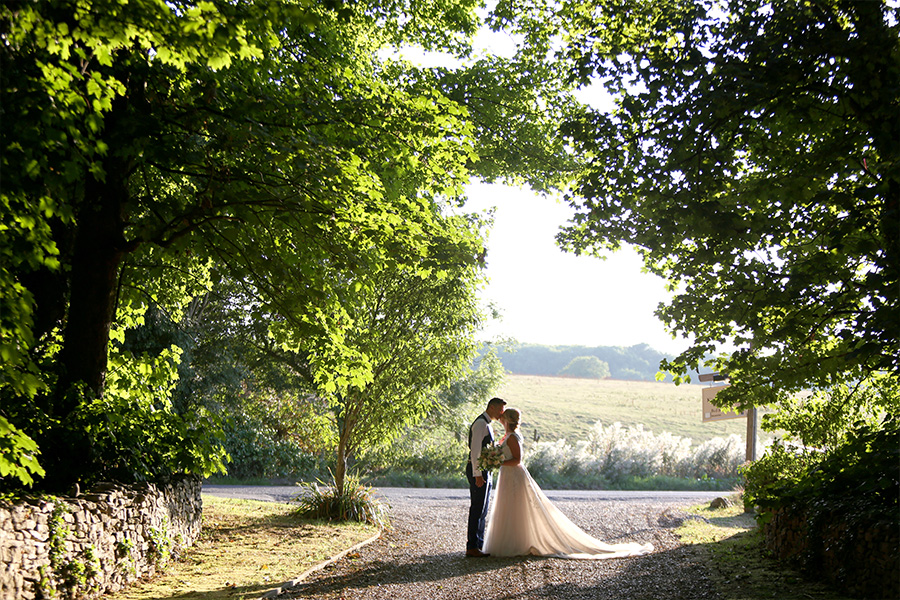 Bride and groom under tree lined path at Kingston Country Courtyard Dorset with countryside views
