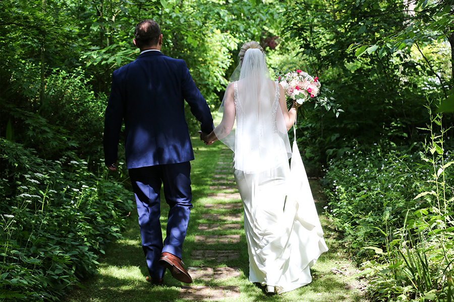 Bride and groom walking through garden path at The Old Vicarage wedding venue Dorset surrounded by greenery