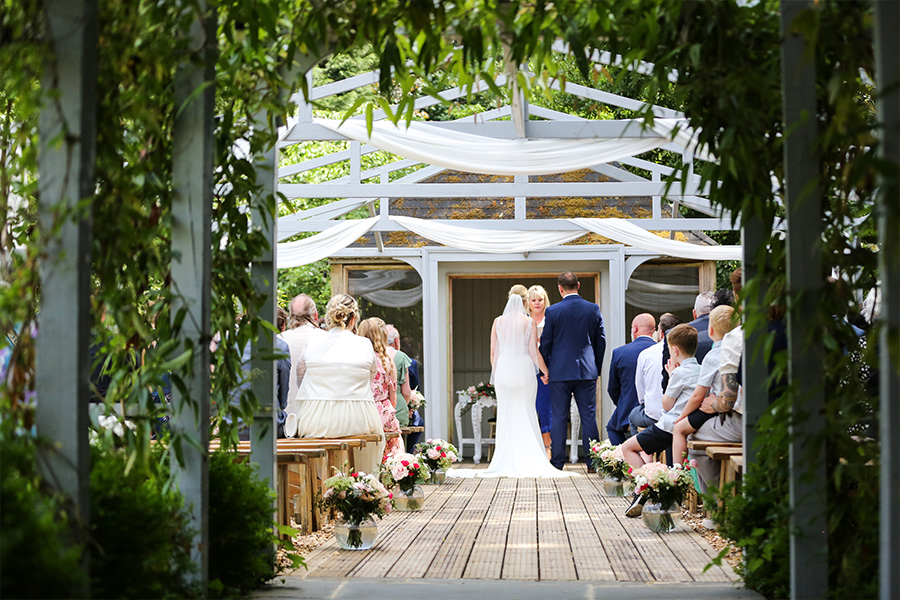 Couple walking down outdoor ceremony aisle at The Old Vicarage wedding venue Dorset with guests and floral decorations