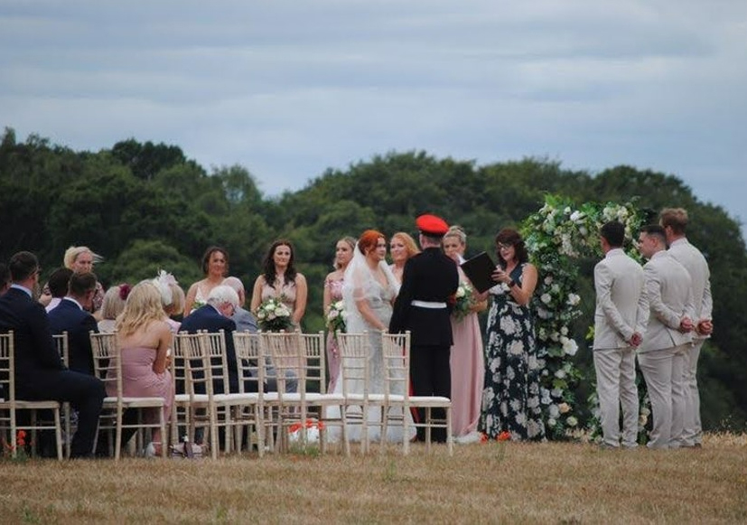 Outdoor wedding ceremony in Hampshire with celebrant leading couple under floral arch