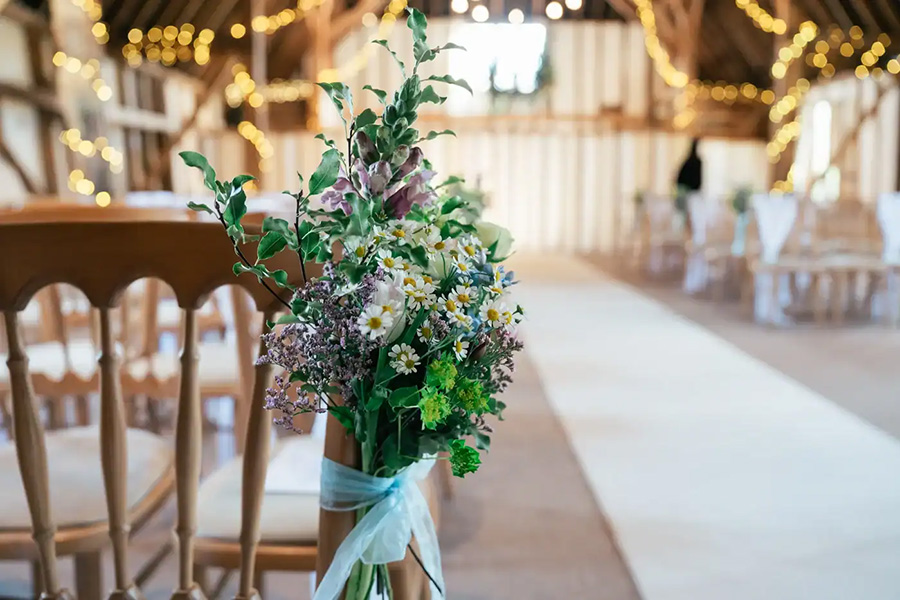 Natural wedding flower arrangement lining ceremony aisle in rustic barn venue Dorset