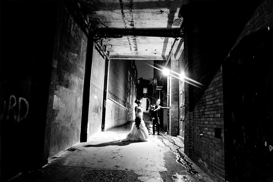 Bride and groom photographed at night in an urban alley with dramatic lighting, capturing authentic wedding storytelling moments