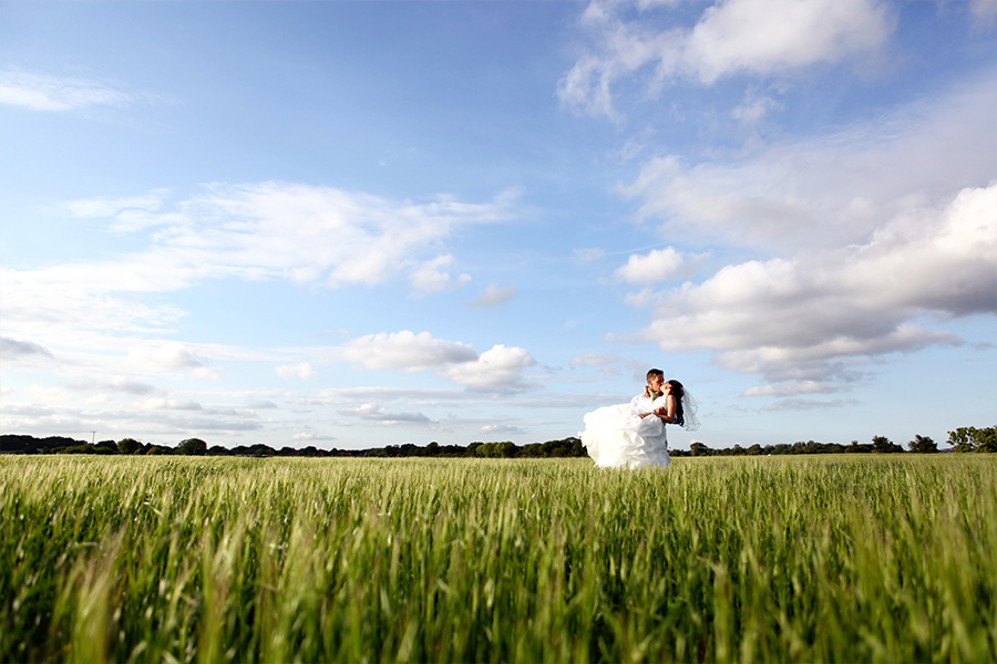 Bride and groom standing in a wide countryside field under a blue sky