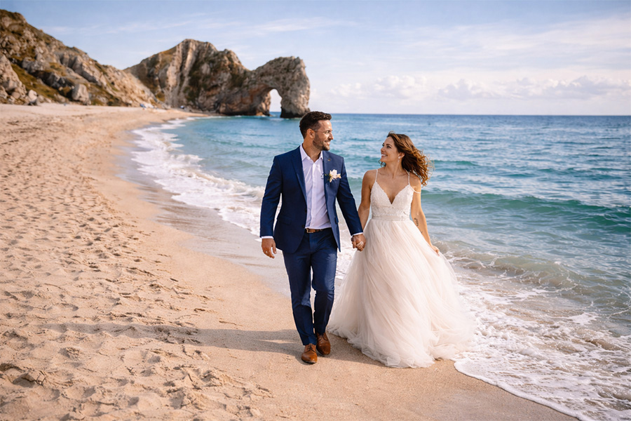 Bride and groom walking along a beach coastline during their wedding day, representing Wiltshire wedding planning and wedding suppliers