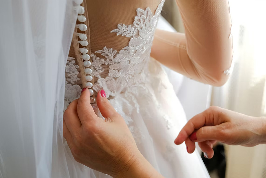 Close up of wedding dress fitting with button fastening detail on lace bridal gown during alteration appointment