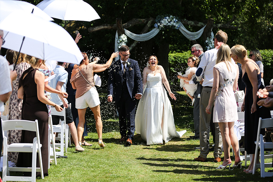 Bride and groom walking through confetti after an outdoor wedding ceremony at Bartley Lodge.