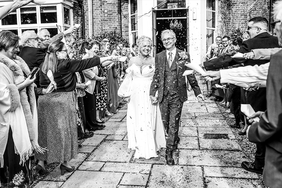 Bride and groom walking through a confetti aisle outside Bartley Lodge wedding venue.