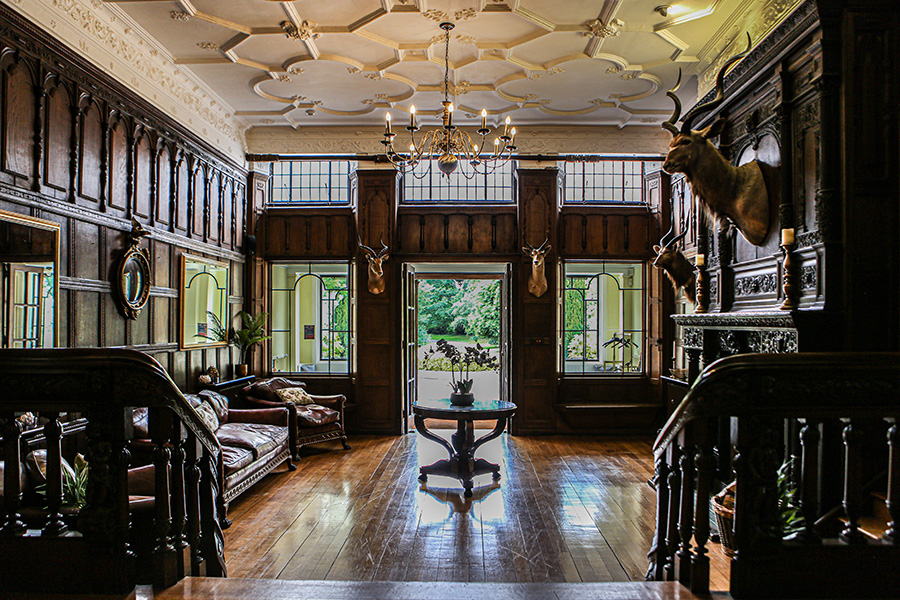 Grand entrance hall inside Efford Park Manor featuring oak panelled walls, ornate ceilings, chandeliers and a sweeping staircase.