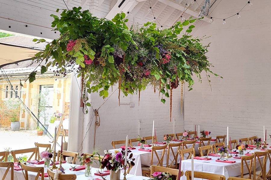 Suspended floral installation by Salisbury wedding florist Coombe Bissett Blooms featuring seasonal flowers and foliage above wedding reception tables