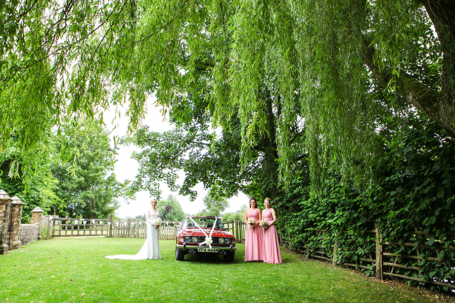 Bride and bridesmaids beside a classic wedding car at a Wiltshire country house wedding venue