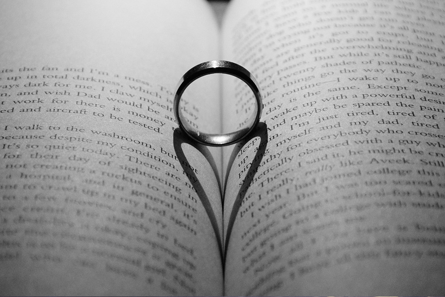 Wedding ring placed on an open book creating a heart shaped shadow